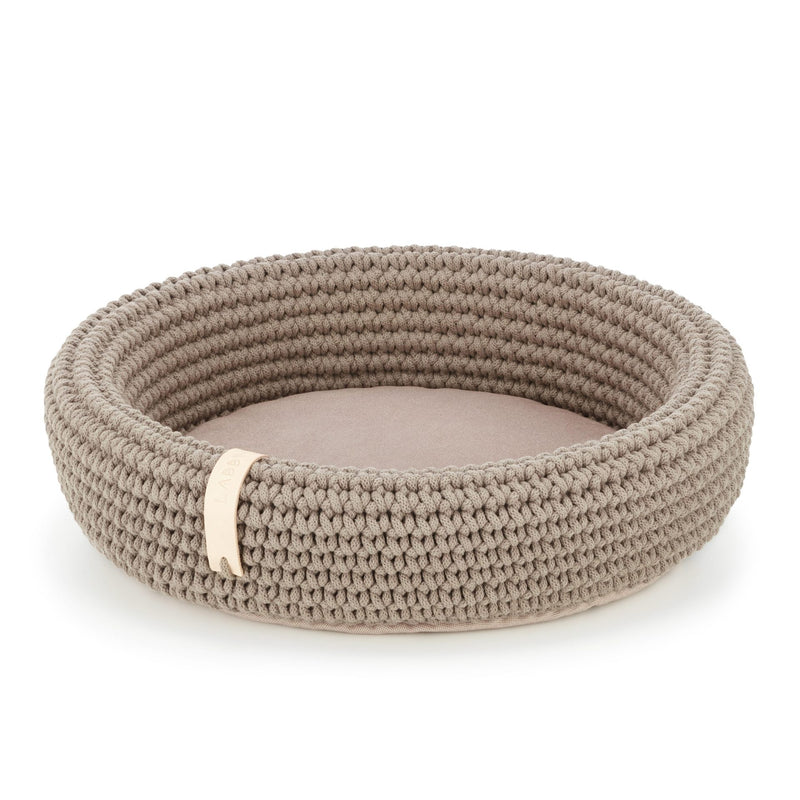 Round woven pet bed with a beige cushion on a white background