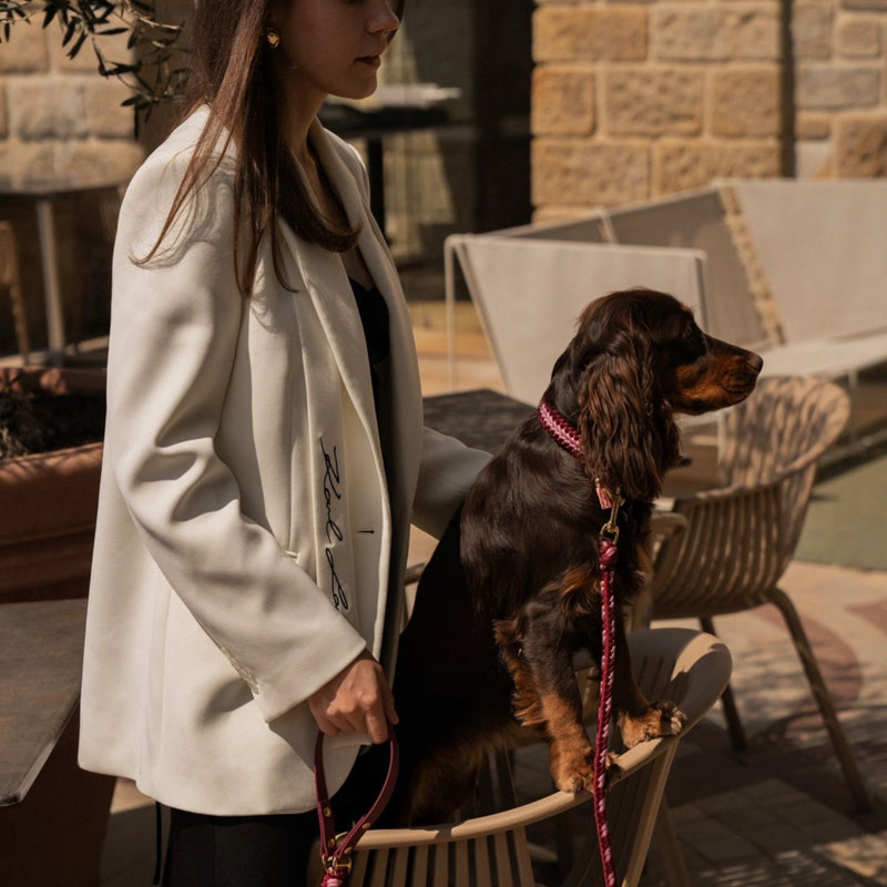 Woman in a white coat with a dog on a leash in an outdoor setting